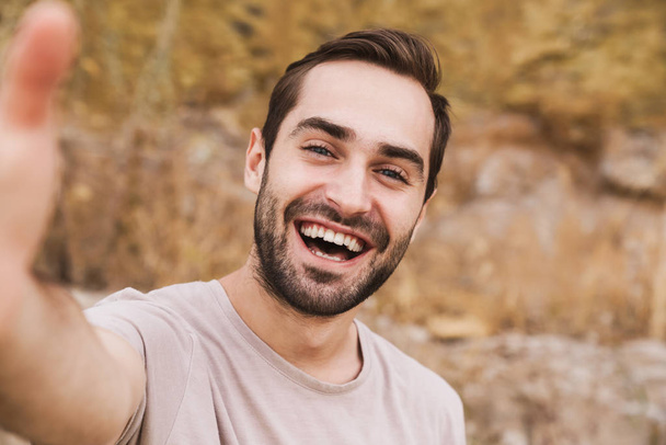 Image of unshaven caucasian man laughing and taking selfie photo - Фото, изображение