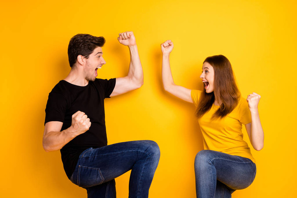 Photo of crazy rejoicing boyfriend and girlfriend overjoyed about sales and discounts where they bought jeans denim black t-shirt isolated over vivid yellow color background - Foto, afbeelding