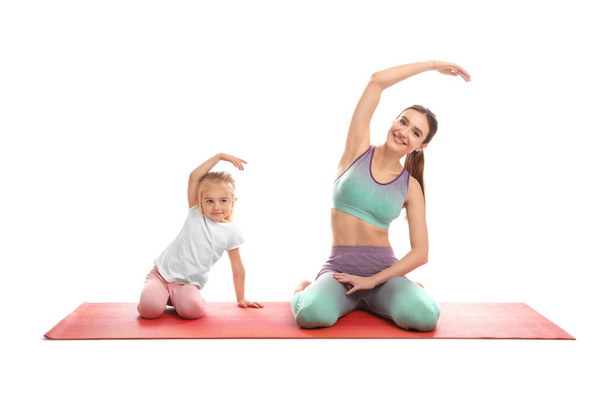 Young woman and her daughter doing exercise isolated on white. Home fitness - Fotó, kép