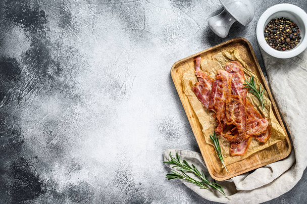 Fried bacon on a wooden tray in Kraft paper. Farm organic pork. Gray background. Top view. Space for text - Fotografie, Obrázek