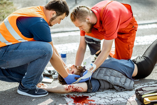 Medics applying emergency care to the injured man on the road - Фото, зображення