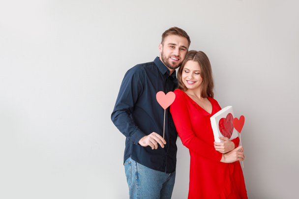 Счастливая молодая пара с сердечками и подарком на светлом фоне. Празднование Дня Святого Валентина
 - Фото, изображение