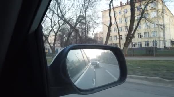 Het uitzicht vanuit de achteruitkijkspiegel is van de auto. Rijden door de drukke straten van de stad. - Video