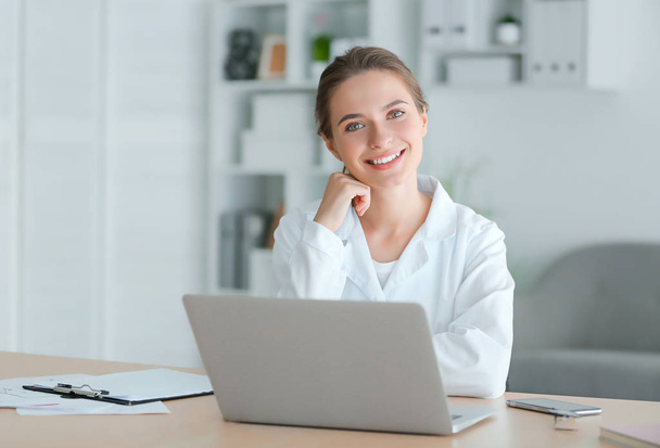 Medico femminile con computer portatile seduto a tavola in clinica
 - Foto, immagini