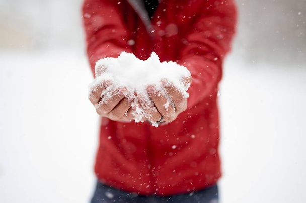 Closeup shot of a male holding snow with his two hands and a blurred background - Foto, imagen