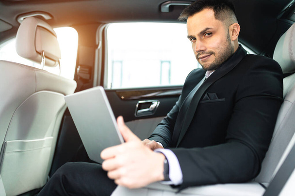 Αυτοπεποίθηση επιχειρηματίας κρατώντας φορητό υπολογιστή στα πόδια, ενώ κάθεται σε εκτελεστικό αυτοκίνητο - Φωτογραφία, εικόνα