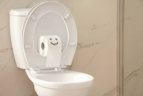 Roll of paper with funny face on toilet bowl in bathroom - Fotoğraf, Görsel
