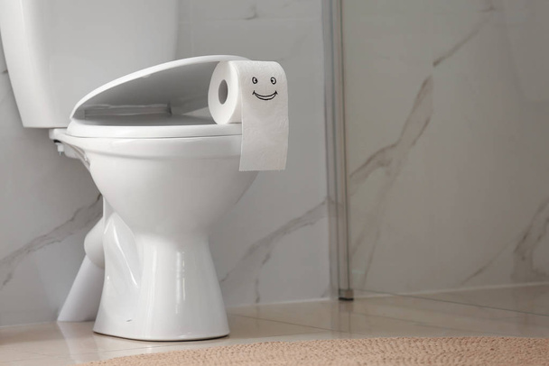Roll of paper with funny face on toilet bowl in bathroom - Фото, изображение