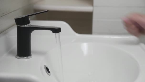 Мужская рука превращает черный кран для воды в раковину в ванной комнате. Вода из крана
. - Кадры, видео