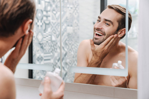 Handsome young shirtless man applying aftershave - Foto, Imagem
