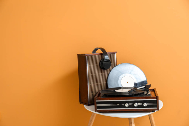Platenspeler, luidspreker, koptelefoon en vinylschijf op tafel in de buurt van kleur muur - Foto, afbeelding