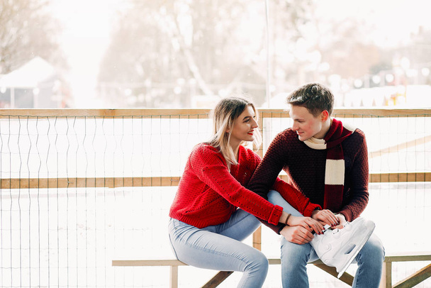 Cute couple in a red sweaters help each other to skate - Photo, Image