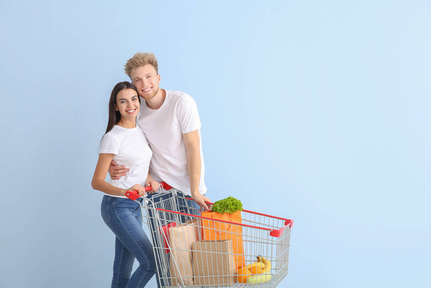 Couple with shopping cart on color background - Photo, Image