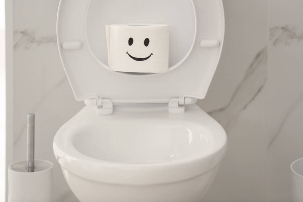 Roll of paper with funny face on toilet bowl in bathroom - Foto, Imagen
