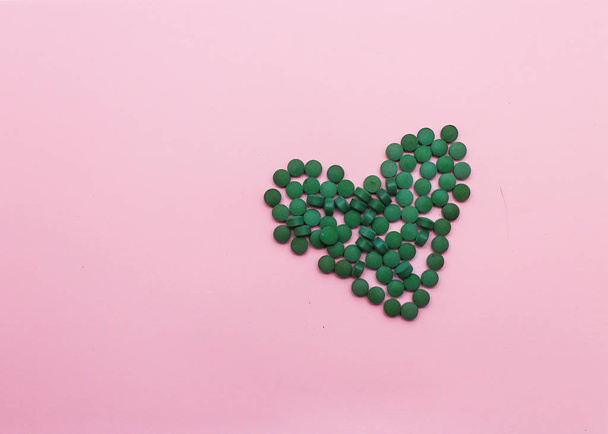 pills laid out in the shape of a heart on a pink background - Valokuva, kuva