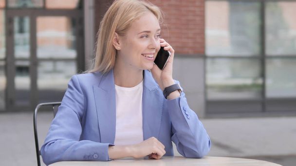 Jonge zakenvrouw praten op telefoon zittend buiten - Foto, afbeelding