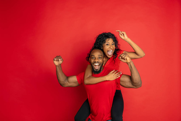 Young emotional african-american man and woman on red background - Фото, изображение