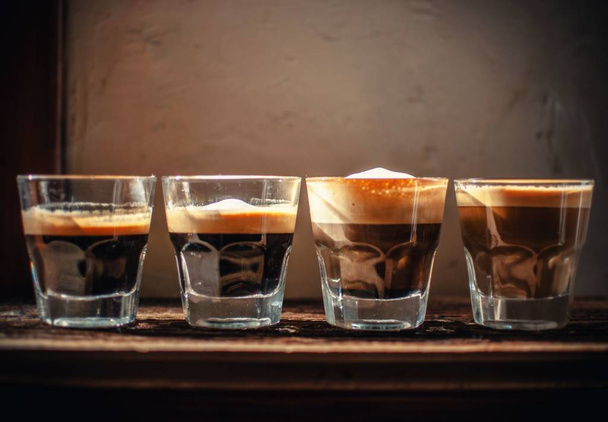 A closeup shot of four glasses with liqueur put in a line on blurred background - Foto, afbeelding