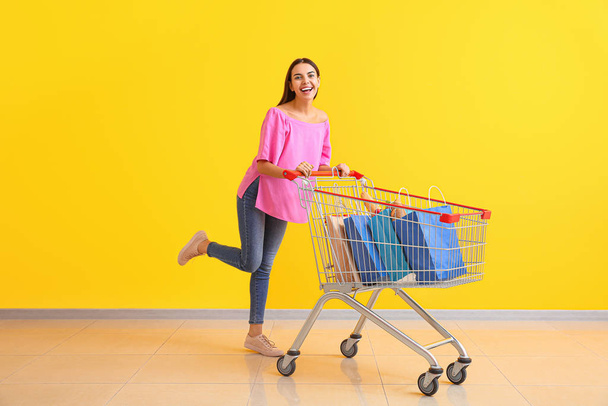 Young woman with shopping cart near color wall - Photo, Image