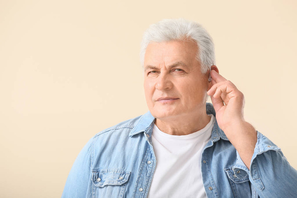 Mature man with hearing aid on light background - Foto, immagini