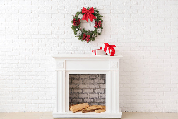 Hermosa corona de Navidad colgando en la pared cerca de la chimenea con cajas de regalo
 - Foto, imagen