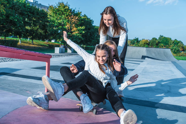 Three teenage girls teenagers ride skateboard, happy have fun playing and laughing, summer sports ground, in warm sweaters fall afternoon. Free space for copy text. Emotions happiness delight. - Photo, Image