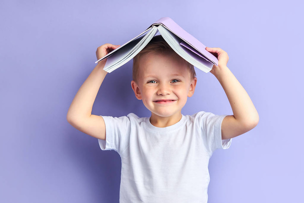 Happy boy with book above head - Фото, изображение