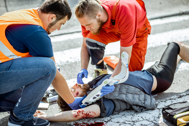 Médicos que aplicam cuidados de emergência ao homem ferido na estrada
 - Foto, Imagem