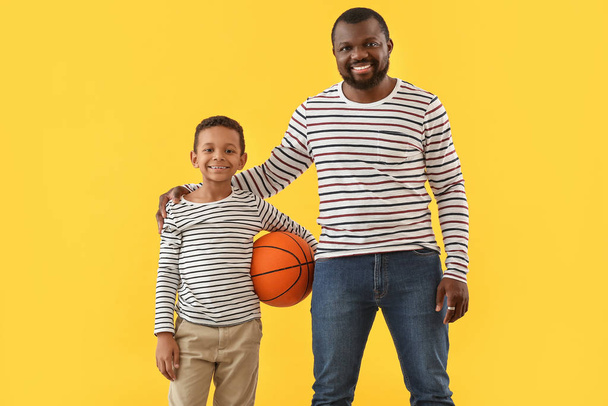 Portrait of African-American man and his little son with ball on color background - Photo, Image