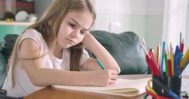 Tired Caucasian girl sitting at the table and doing homework. Exhausted child laying down head on exercise book and closing eyes. Overworking, studying, education concept. Cinema 4k ProRes HQ. - Materiał filmowy, wideo