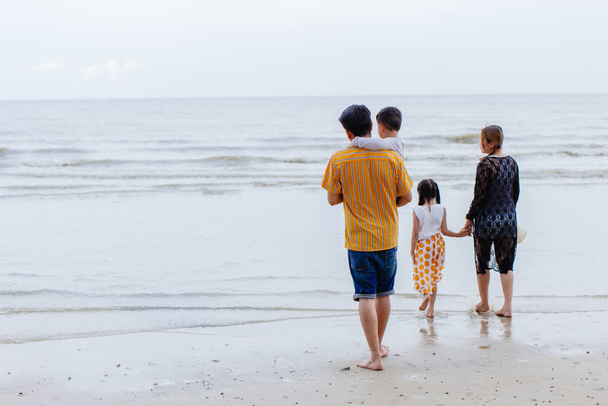 Familia asiática padres con hija e hijo caminando en la playa del mar para vacaciones de verano con espacio para el texto
. - Foto, imagen