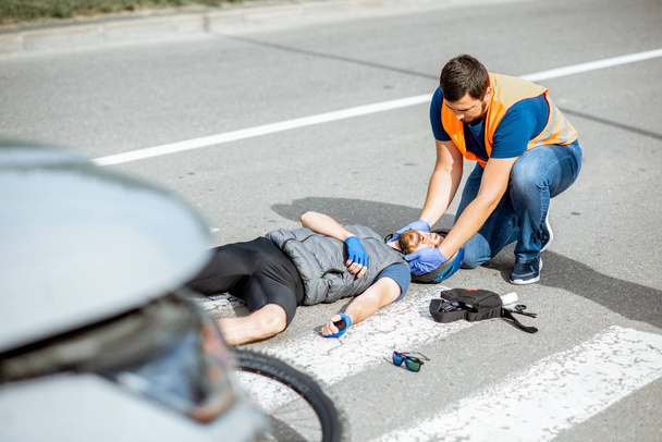 Liikenneonnettomuus loukkaantuneen pyöräilijän ja ensiapua antavan miehen kanssa
 - Valokuva, kuva