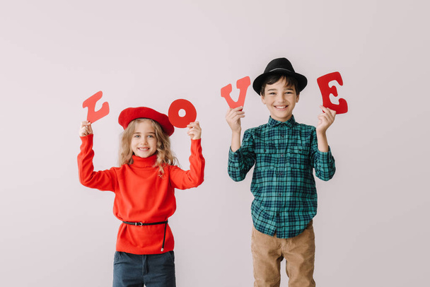 Lindos niños pequeños con palabra AMOR sobre fondo gris. Celebración de San Valentín
 - Foto, imagen