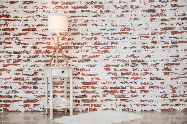 Table élégante avec lampe lumineuse près du mur de briques dans la chambre
 - Photo, image