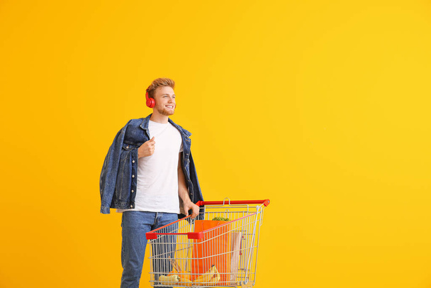 junger Mann mit Einkaufswagen auf farbigem Hintergrund - Foto, Bild