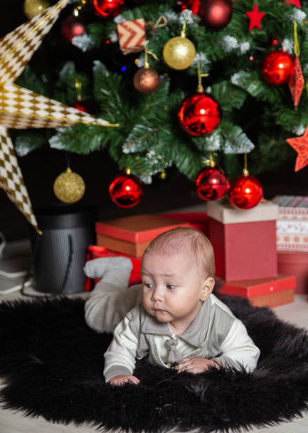 Słodki chłopczyk na podłodze przy drzewie Nowego Roku. - Zdjęcie, obraz