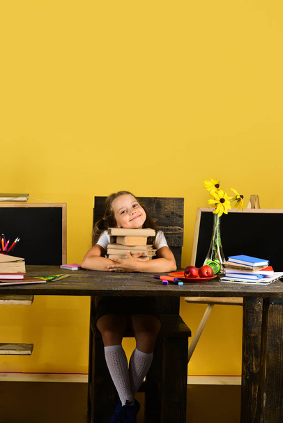 Girl sits at desk with colorful stationery, flowers and fruit - Fotó, kép