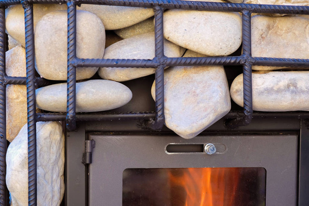 Frammento di un forno con fiamme e pietre dietro una grata in metallo. Bathhouse
. - Foto, immagini