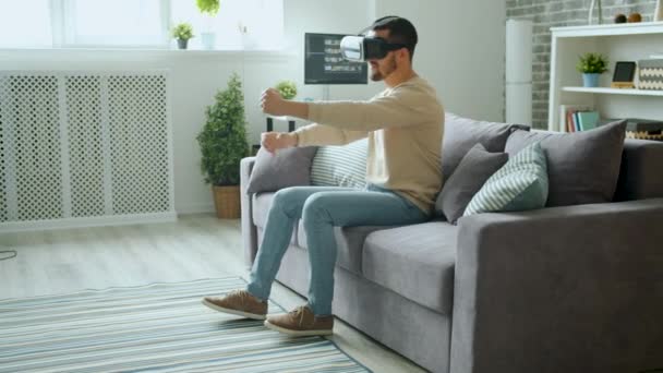 Joyful man enjoying driving in vr goggles having fun at home with modern device - Imágenes, Vídeo