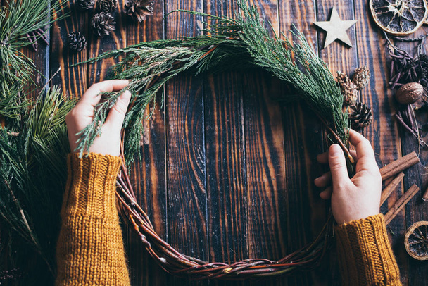 Female hands making Christmas wreath on dark wood background - Fotoğraf, Görsel