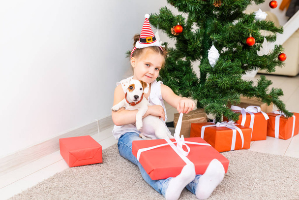 Vánoce, domácí mazlíčci a dovolená koncept - Dítě v santa klobouku s jack Russell teriér štěně - Fotografie, Obrázek