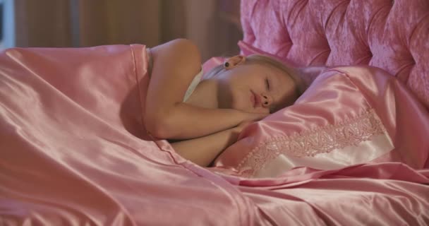 Close-up of cute Caucasian little girl sleeping in pink bed. Tired child resting at home. Carefree childhood. - Footage, Video