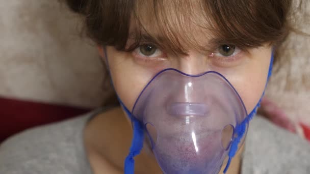 Egy nő kék kórházi maszkban. Belégzés gőzök a légutakból a tüdőbe. Köhögés elleni kezelés. Egy maszkos beteg lány belélegzett egy spray-s üveget. Közelkép - Felvétel, videó