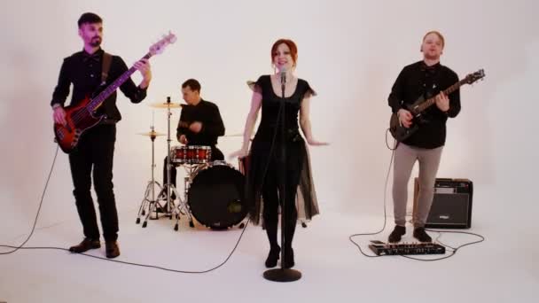 Een muzikale band van vier mensen in zwarte kleren die in de heldere studio een lied spelen - Video