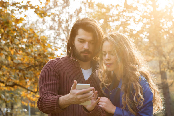 Mladý pár pomocí mobil na podzim barevný park. - Fotografie, Obrázek