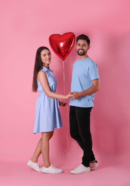 Lovely couple with heart shaped balloon on pink background. Valentine's day celebration - Фото, изображение