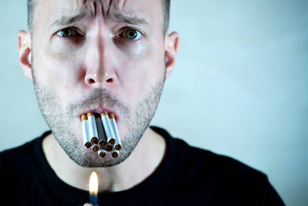 a man with a suffering face holds a lot of cigarettes in his mouth and looks at the camera, copy space - Φωτογραφία, εικόνα