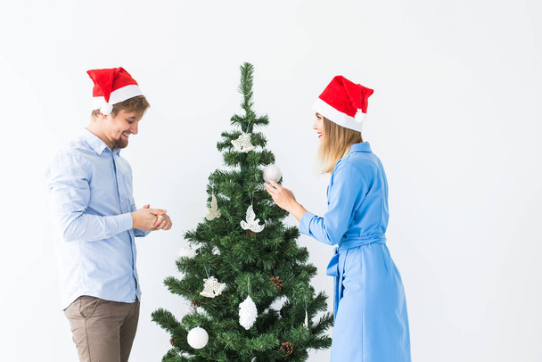 Holidays and festive concept - Young family couple in santa hats decorating the christmas tree - Photo, Image