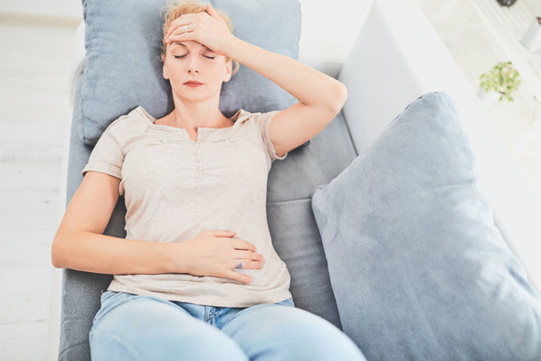 Woman with  stomach issues / problems while lying on the couch. - Photo, image