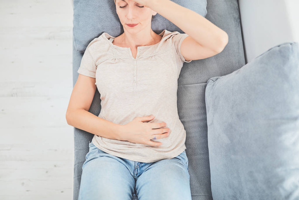 Woman with  stomach issues / problems while lying on the couch. - Photo, Image